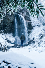 People at the Blue water in winter with snow falling, icicle in the water, trees and a big waterfall