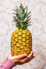 A woman in the room holds a ripe tasty pineapple in her hands_