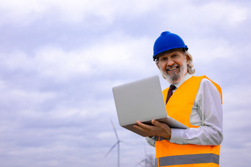 Senior wind turbine engineer with laptop in safety gear on the field