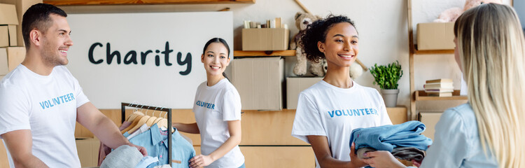 panoramic shot of smiling multicultural volunteers giving clothes to woman