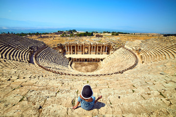 Back view of woman traveler in hat looking at amazing Amphitheater ruins in ancient Hierapolis,...
