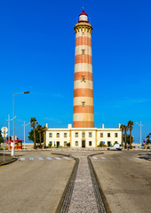 Fototapeta na wymiar Lighthouse of Praia da Barra during the day, with a clear blue sky. View of the lighthouse of Barra beach (Praia da Barra) in Aveiro, Portugal.