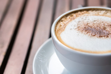 Hot coffee placed on the wooden table in early morning with copyspace, white cup and silver spoon. The green background with defocus effect.
