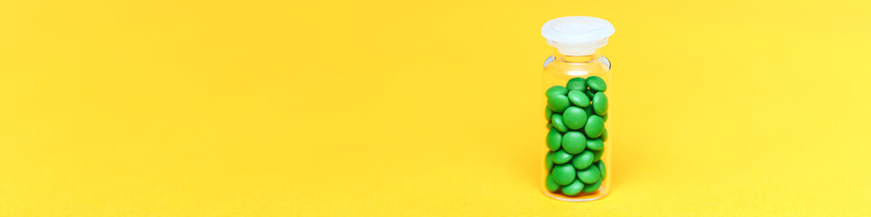 Medical green pills in a glass bottle on yellow background copyspace, health