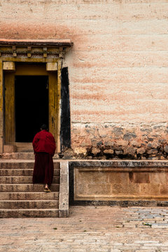 Ein M&ouml;nch steigt im roten Gewand die Treppen ins Kloster 