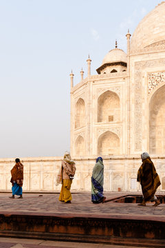 Vier Frauen in Gewändern laufen vor dem Taj Mahal im Sonnenaufgang 