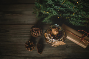 Christmas gift, spices and decor in the glass jar, pine cones, fir branches on wooden brown background. Copy space for your text. Holidays, winter, Christmas presents concept. Toned image. Soft focus.