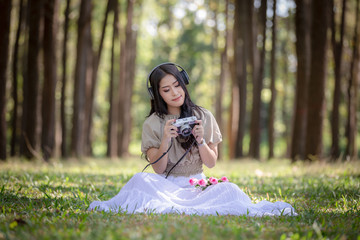 woman asian girl sitting relax listening to music on headphones Bluetooth and camera shooting on hand in the park © SHUTTER DIN