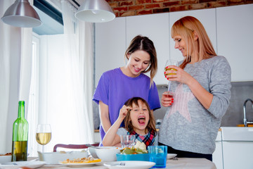Young lesbian family with a girl at kitchen.