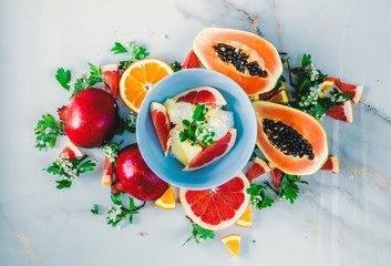 Fresh cut papaya with ceeds, garnets, oranges near ice-cream on marble surface. Above view