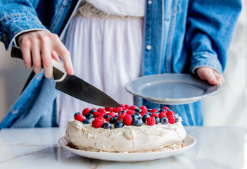 female hands of the pastry chef cut cream pie with blueberries and raspberries on a table