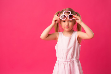 happy baby girl smiling in sunglasses on pink background. the concept of childhood