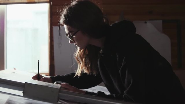 Concentrated young stylish female engineer, designer or artist drawing the project on a desk in modern light office. Creation, talent, working hard. Professionalism, sketching the plan Female portrait