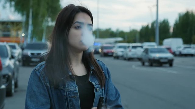 Serious cute girl vaping on the parking near the mall
