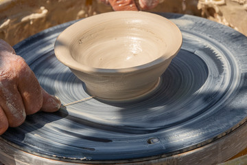 Potter cuts the finished clay vase from the spinning wheel. Summer outdoor potter lessons