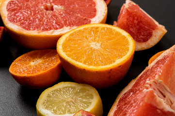 Naklejka na ściany i meble Close up. Colorful slices juicy grapefruits, oranges on a black background. Ingredients.