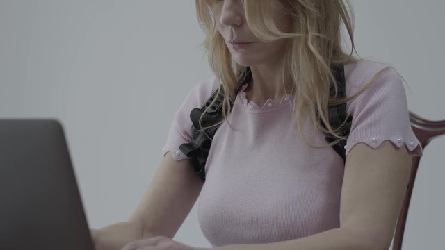 Close up portrait pretty slim blond woman in an orthopedic corset for the back sit on the table and working at laptop computer