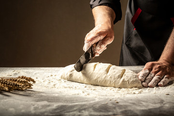 Baker making patterns on raw bread using a knife to shape the dough prior to baking. Manufacturing...
