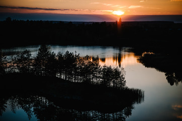 Sunset on lake, landscape. Autumn nature. Island for fishing in the middle of the lake. Colorful sky and water in lake reflected in evening.