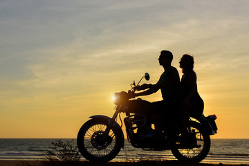 Fototapeta na wymiar Silhouettes of guy and girl on motorcycle on sunset background. Young couple are sitting on motorcycle, faces in profile.