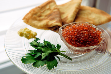 Red salmon caviar with pancakes and parsley on a glass plate, selective focus.