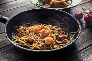 Pasta spaghetti on plate and pan with shrimp tomato sauce toatoes and herbs. Italian or mediterranean cuisine