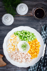 Corn salad, cucumber, egg, chicken on a white plate on a black table, top view, selective focus