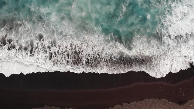 Areial view of blue waves crashing into the black sand beach