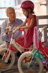 Obraz premium Happy child girl sits on bicycle in bike shop.