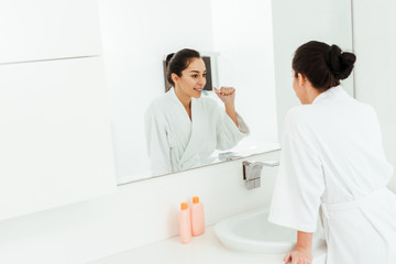 selective focus of cheerful woman looking at mirror while brushing teeth in bathroom