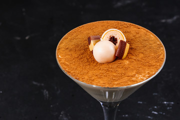 Traditional Italian dessert tiramisu, decorated with chocolate, candy and toffee, in a martini glass, on a black background