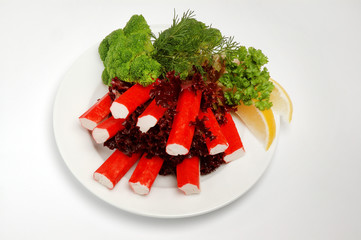 Crab sticks on a plate with salad, lemon slices on a white background