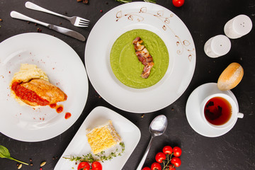 Multi-course business lunch: mashed potatoes with chicken breast, Russian traditional salad, green pea puree bacon  with black tea, on black background
