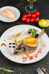 stuffed fish with carrots, parsley, horseradish and salad on a white plate, with tomatoes, lime, fork and knife, with a glass of white wine on a black background