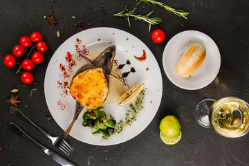 Fototapeta na wymiar stuffed fish with carrots, parsley, horseradish and salad on a white plate, with tomatoes, lime, fork and knife, with a glass of white wine on a black background