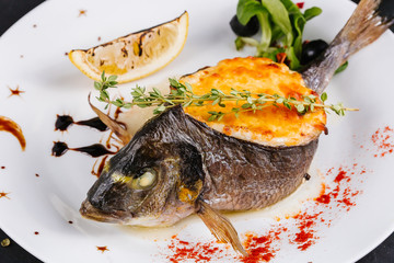 stuffed fish with carrots, parsley, horseradish and salad on a white plate, with tomatoes, lime, fork and knife, with a glass of white wine on a black background