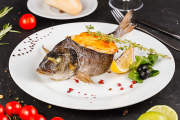 stuffed fish with carrots, parsley, horseradish and salad on a white plate, with tomatoes, lime, fork and knife, with a glass of white wine on a black background