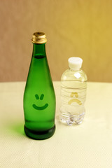 Green glass and plastic bottles of drinking water with painted smilies