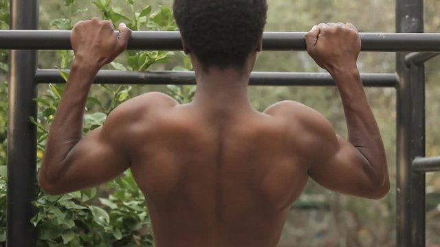 Poor african guy making gym outdoors. muscular man pulling up on horizontal bar