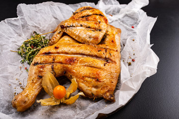Grilled chicken Tabaka served with herbs on black background. Macro.