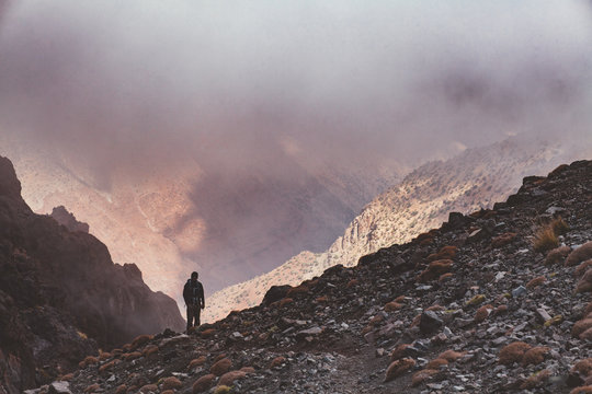 einsamer Wanderer in den Bergen des Atlas Gebirges, der in eine Schlucht voll mit Nebel schaut.