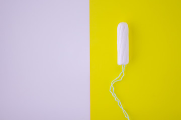 One swab with cotton on a yellow background. The concept of the period of the menstrual cycle. Top view, flat lay.