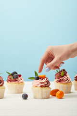 partial view of woman with sweet cupcakes with berries