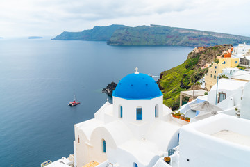 Traditional whitewashed church with blue dome in Oia with view of caldera and Aegean Sea. Santorini, Greece