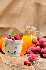 Yoghurt with oatmeal and fresh raspberries in a glass and mint leaves, full glass of oatmeals and orange juice in background - vertical photo