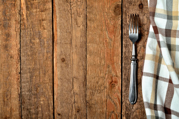 Checkered tablecloth right frame and fork on vintage wooden table background - view from above