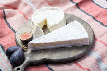 Two pieces of French soft cheeses Brie and Camembert with white mold and strong odor, served with fresh ripe figs