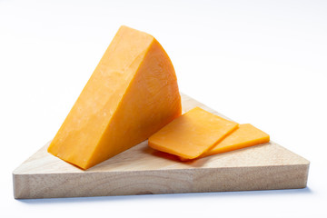 Piece of hard orange Cheddar cheese on wooden cheese plank isolated close up