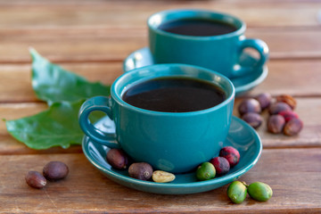 Cup with black coffee served outside with raw green, mature red and roasted coffee beans, decorated with green leaves from coffee plant