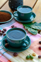 Cup with black coffee served outside with raw green, mature red and roasted coffee beans, decorated with green leaves from coffee plant